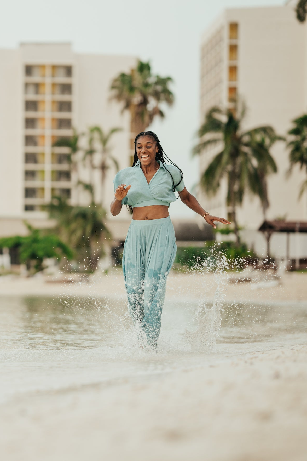 Woman in a mint two-piece runs laughing through shallow water at Secrets Wild Orchid Montego Bay