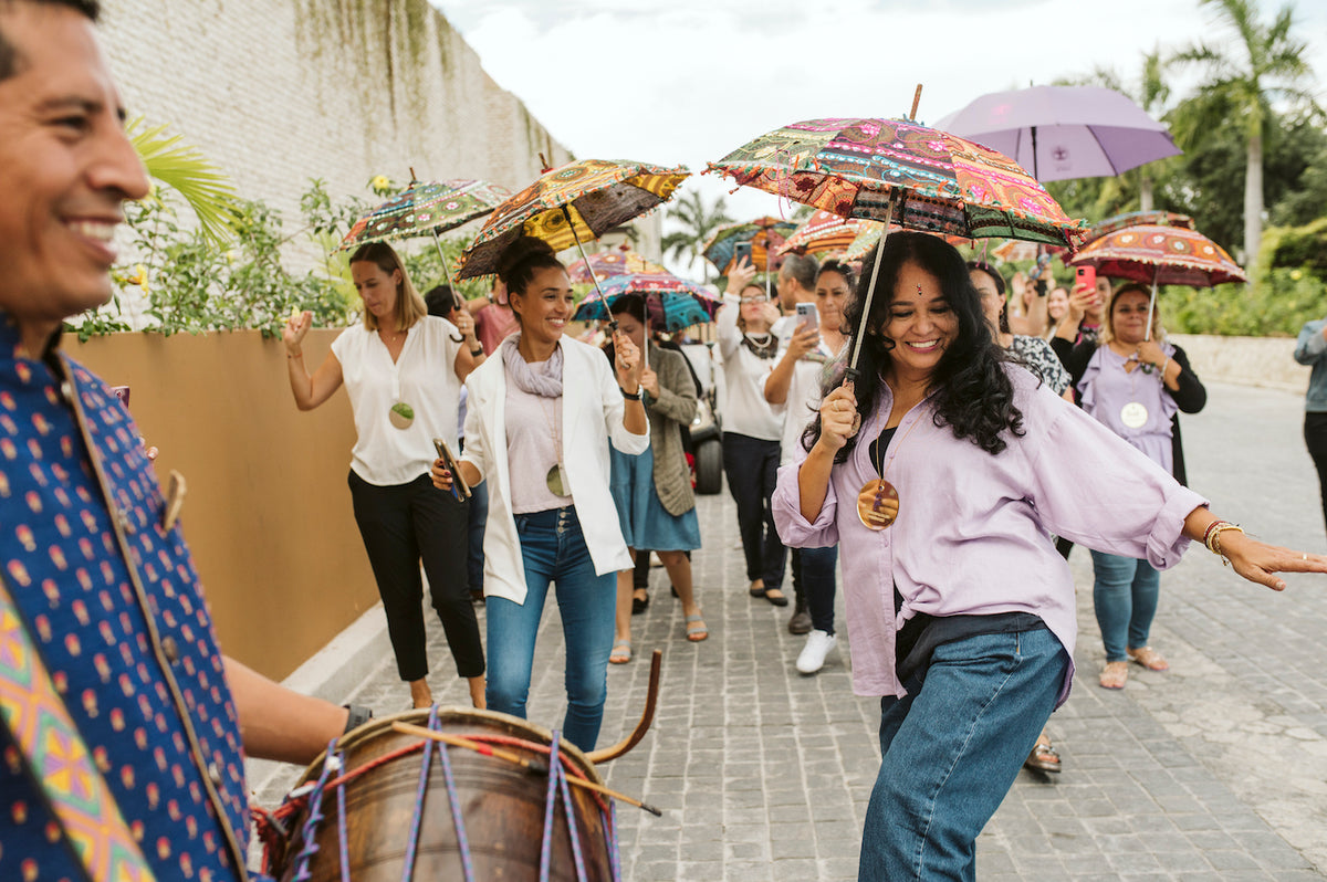 Women dance under embroidered parasols behind a dhol drummer during a South Asian wedding certification parade
