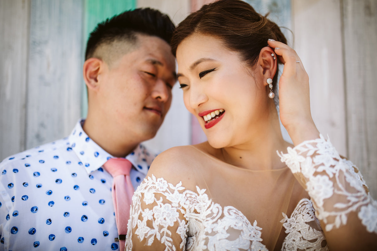 Laughing bride in a lace gown and groom with a pink tie lean together at Thompson Playa del Carmen