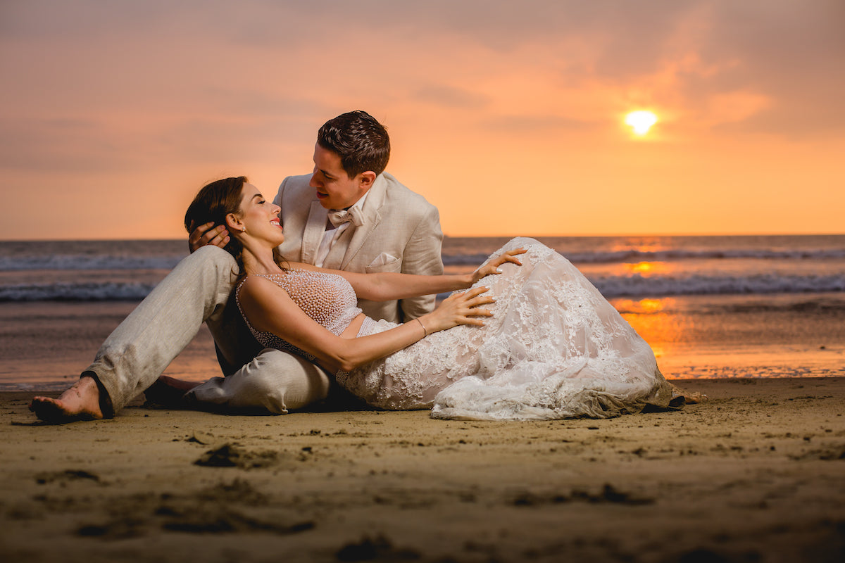 Bride and groom recline on wet sand at sunset during an ocean trash the dress photoshoot