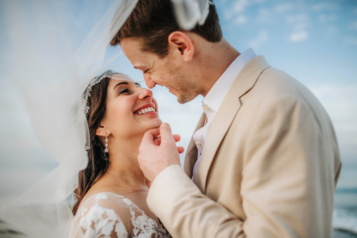 Groom tenderly lifts the bride's chin beneath her windswept veil at Viceroy Riviera Maya