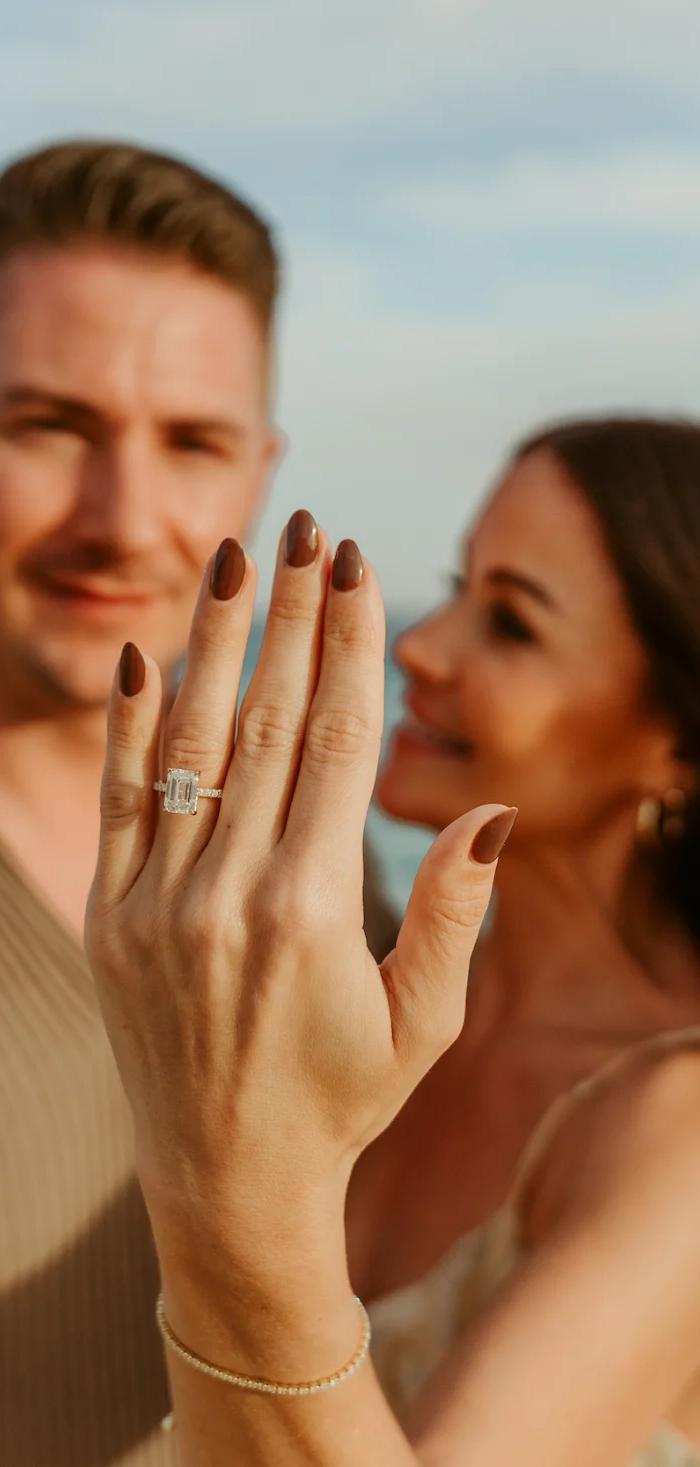 A newly engaged woman shows her ring beside her fiancé on the beach