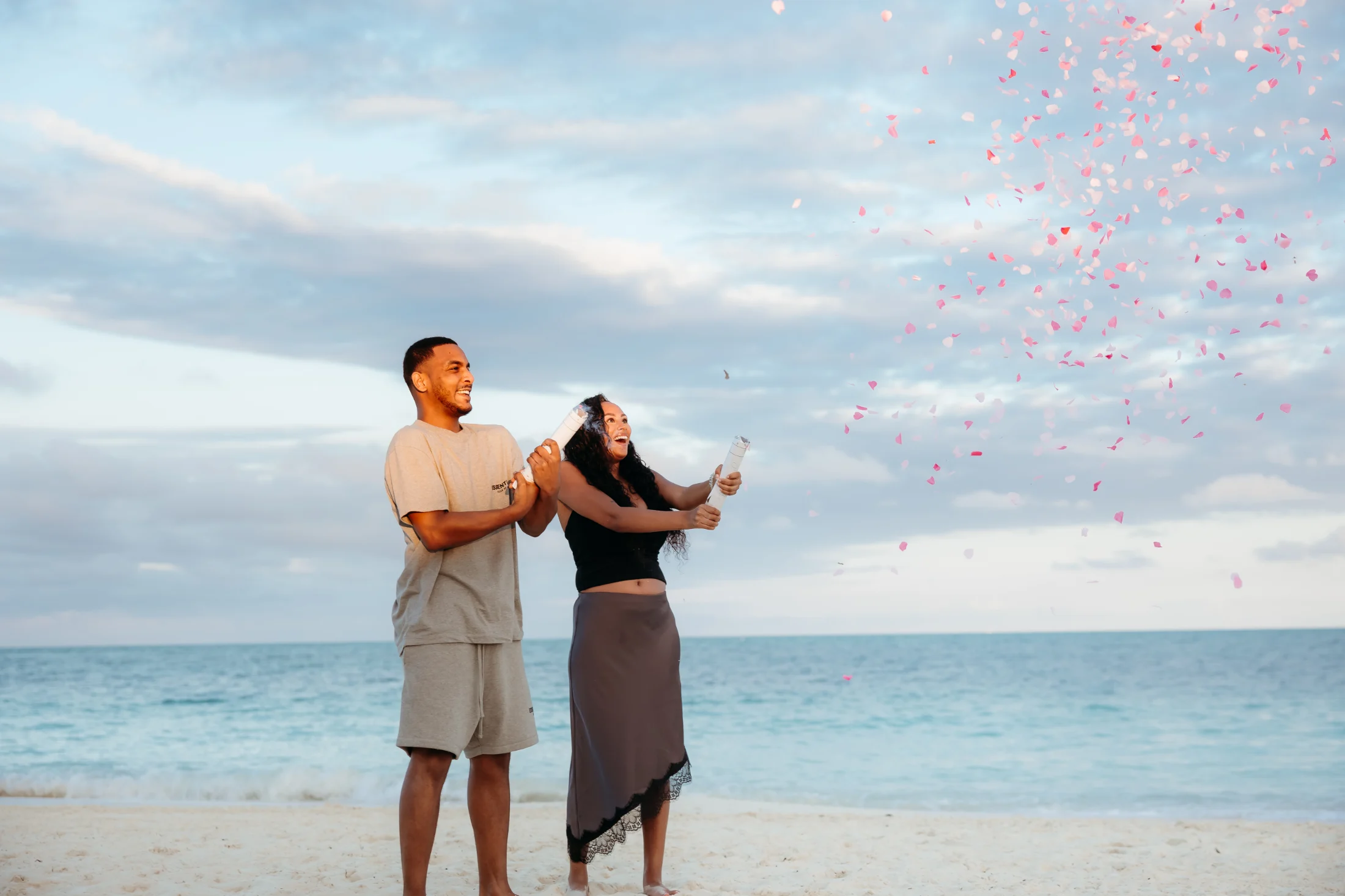 Couple on the beach as pink confetti bursts for their gender reveal