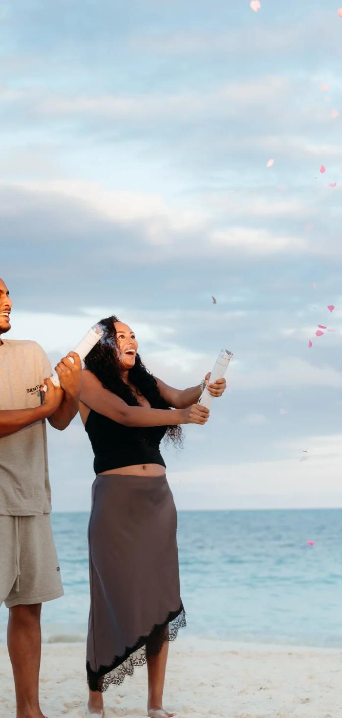 Couple on the beach as pink confetti bursts for their gender reveal