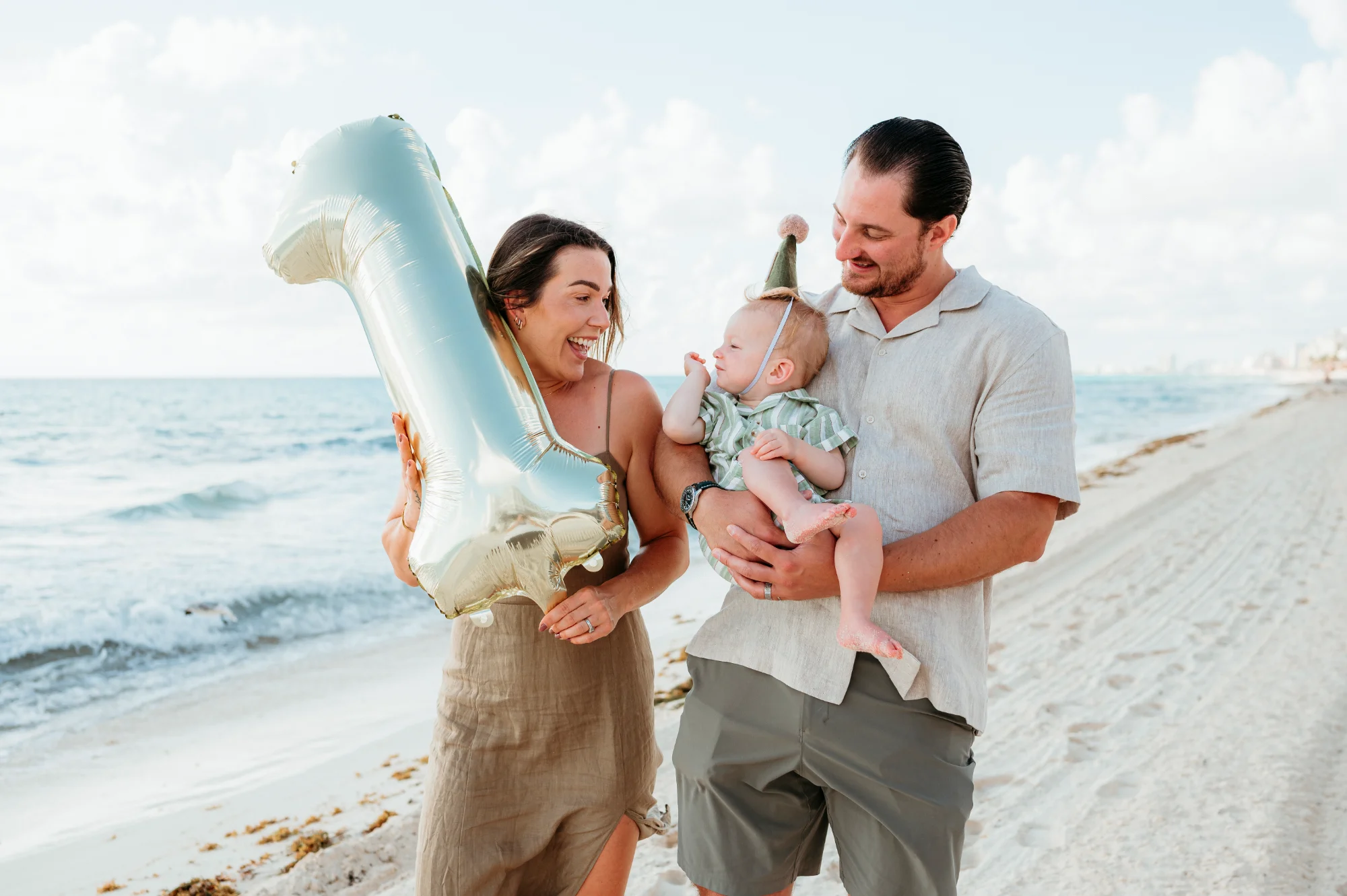 Parents on the beach with their baby and a number one balloon for a first birthday