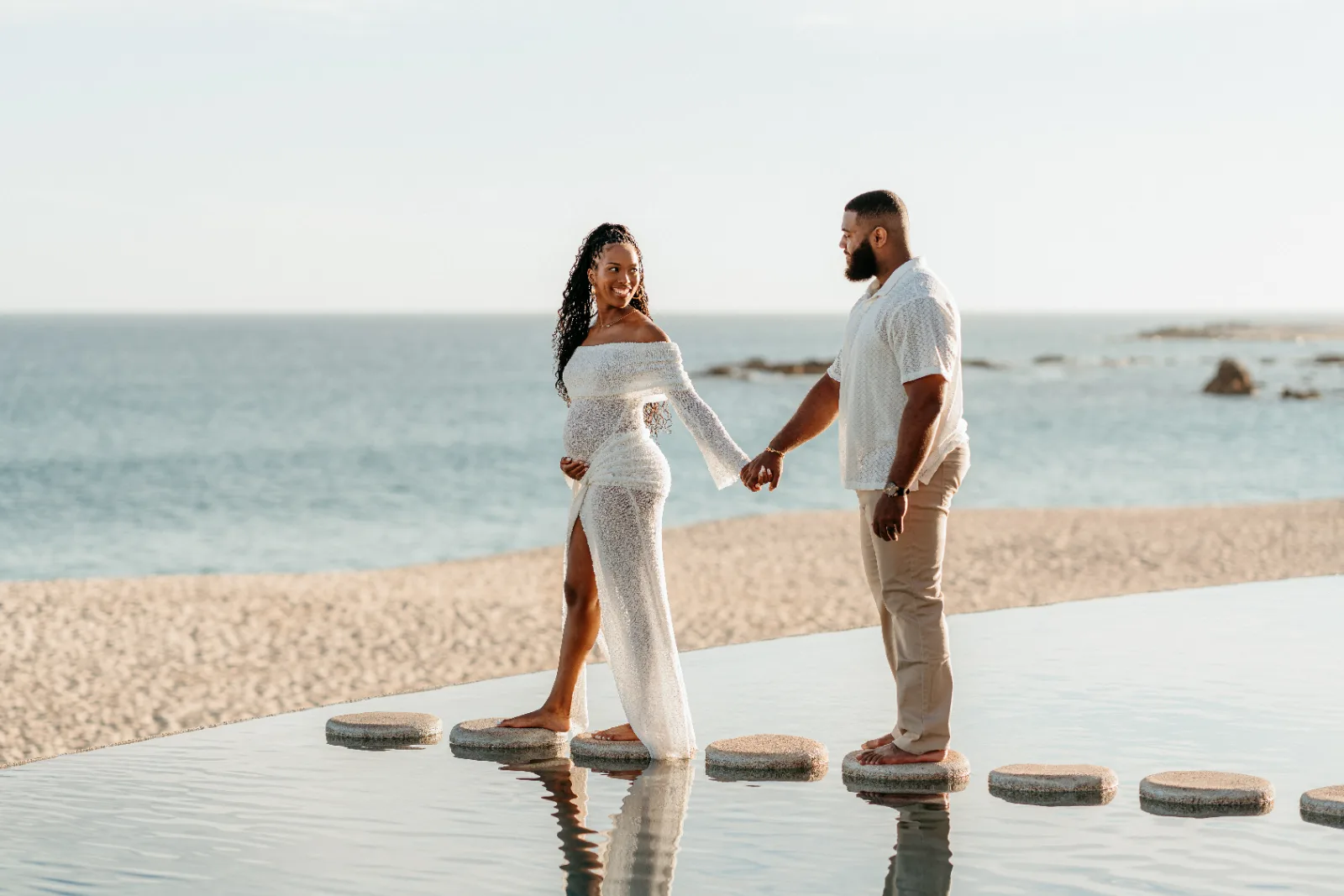 Parents-to-be hold hands on stepping stones by the sea