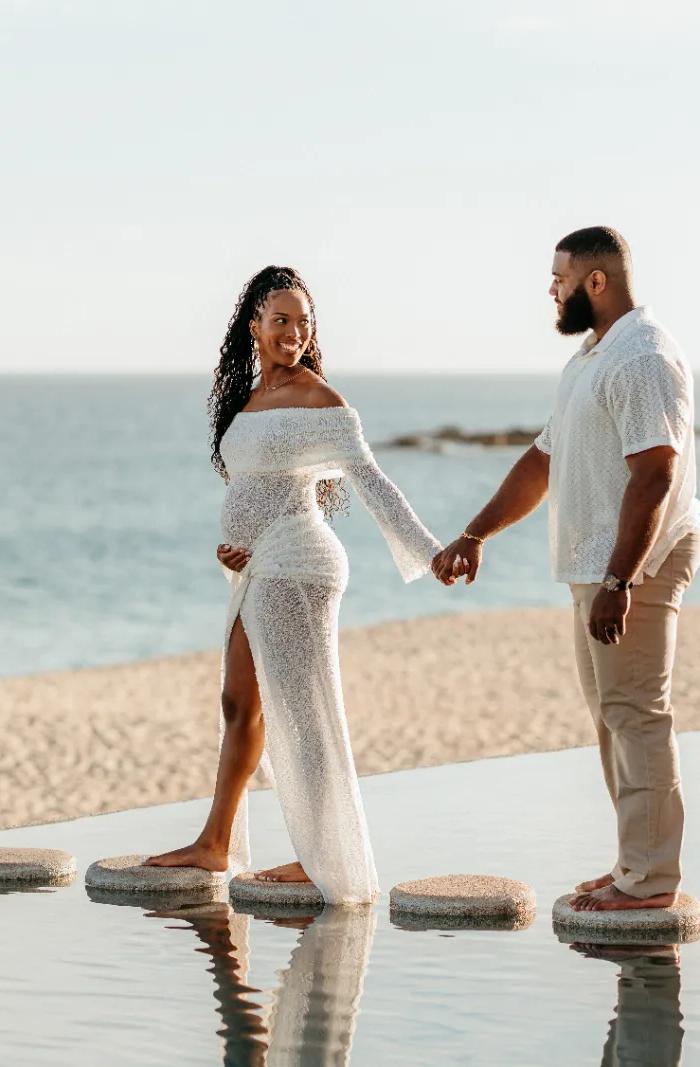 Parents-to-be hold hands on stepping stones by the sea